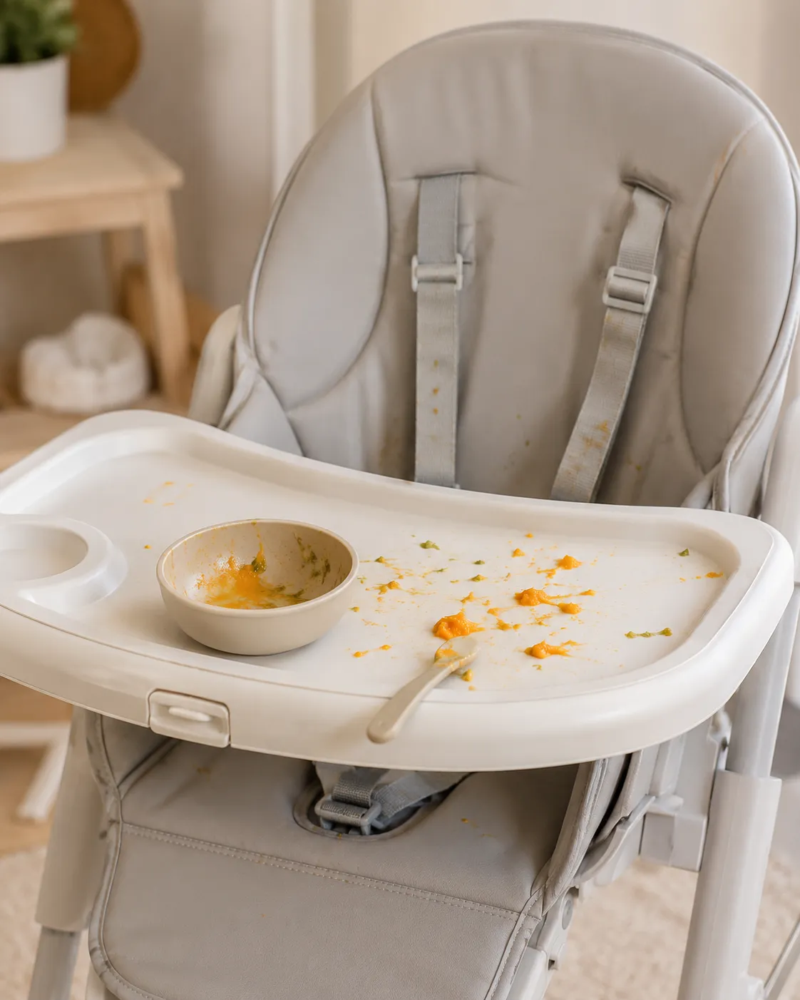 Bol de purée de carotte orange posé sur le plateau d'une chaise haute, avec quelques éclaboussures, scène réaliste d'un premier repas de bébé